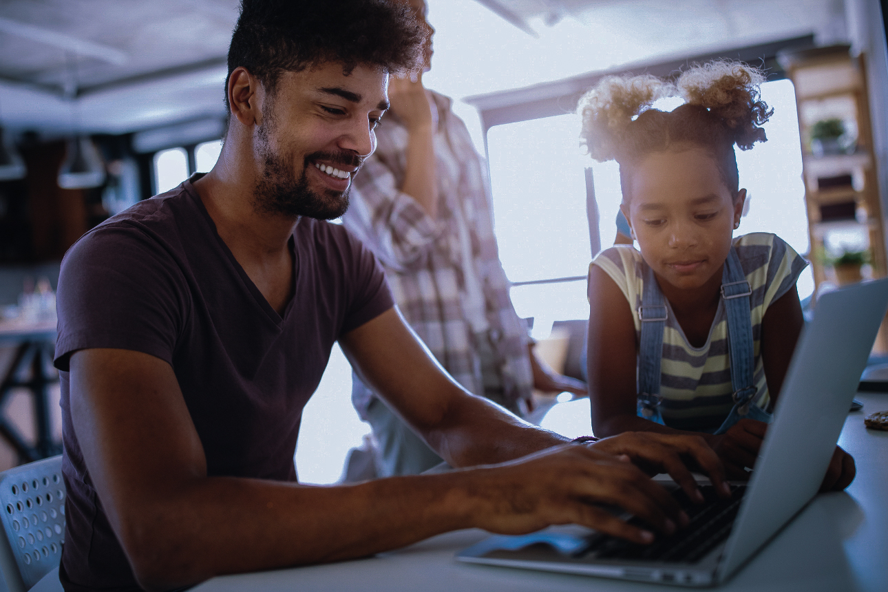 father and child looking at each other smiling while on laptop